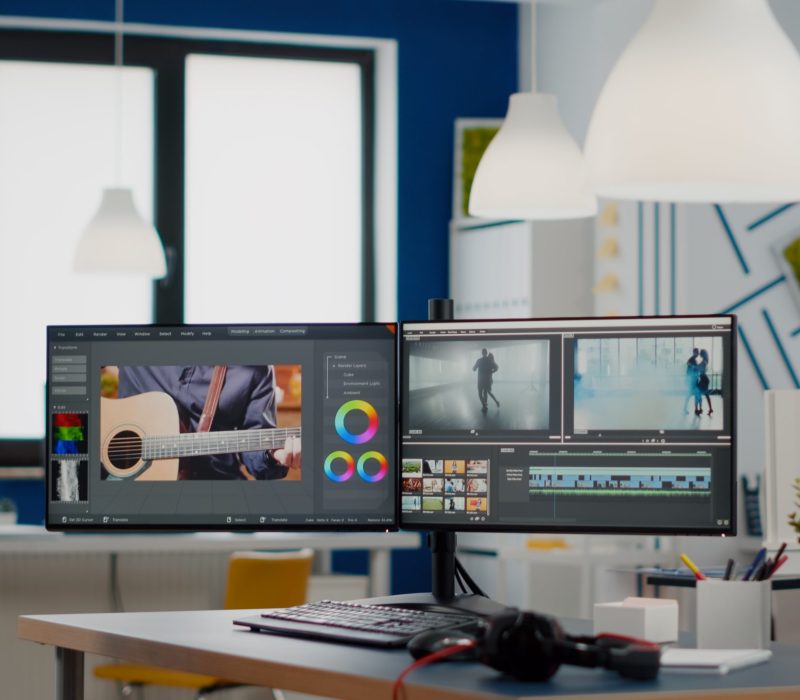 Empty modern creative agency office with dual monitors setup with processing video film montage. Video editing start up studio company with no people in it and post production software on pc displays